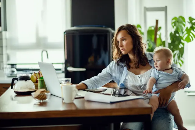 Jeune mère travaillant sur son ordinateur tout en portant son bébé