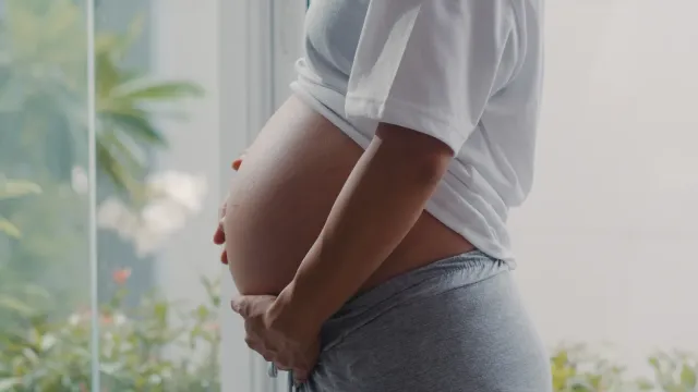 Femme enceinte tenant son ventre arrondi près d'une fenêtre