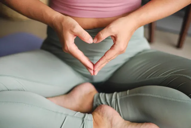 Femme assise en position de yoga, les mains formant un cœur, dans une posture de bien-être
