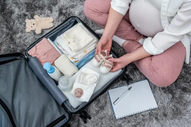 Future maman préparant sa valise de maternité, vue de dessus : vêtements de bébé, chaussons et check-list